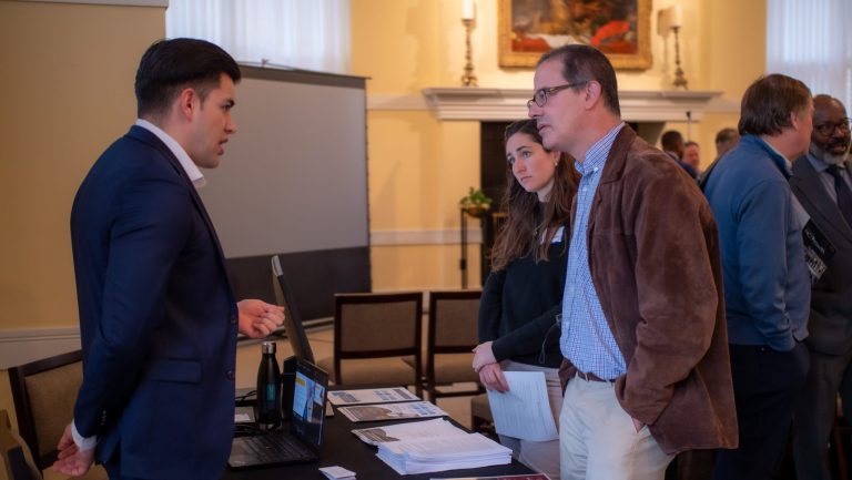Student presenter at a information table talking about NCGrowth to two other people.
