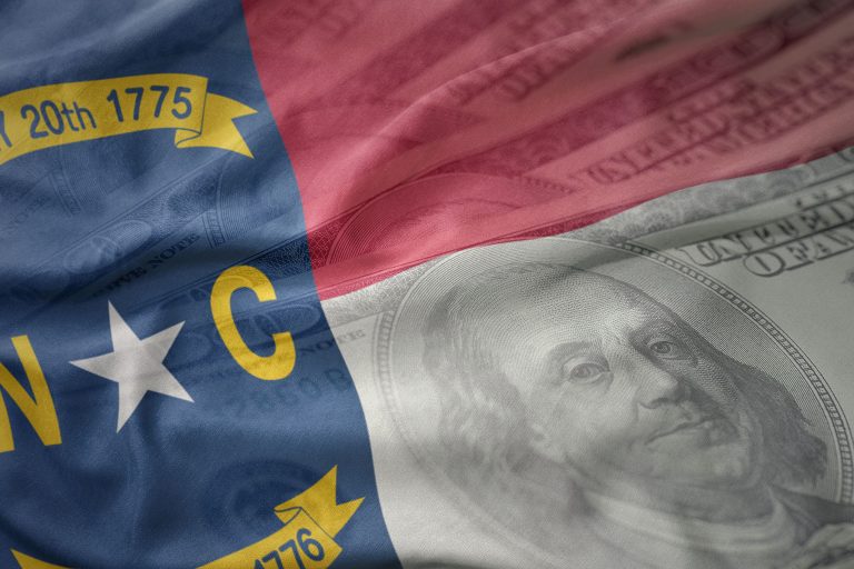 North Carolina state flag overlaid with a faint image of a U.S. hundred-dollar bill